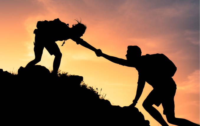 A hiker helps another person climb a rocky slope